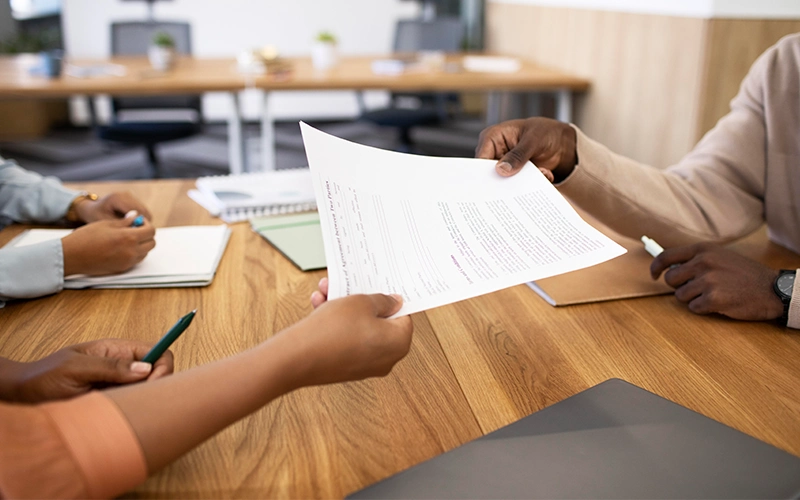 a person is typing on a paper while a woman sits at a desk.