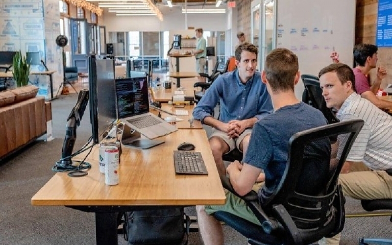 Three man sitting at a table with a laptop.